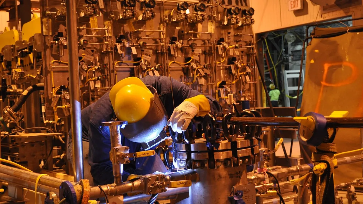 Welder repairing pipe work beside a valve installation in a workshop